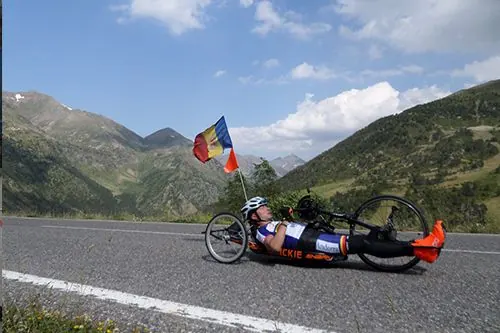 Esportista amb handbike en una carretera de muntanya amb la bandera d'Andorra